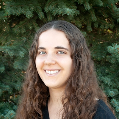 Staff Member At Live Well Chiropractic Anne Smiling In Front Of Fir Tree