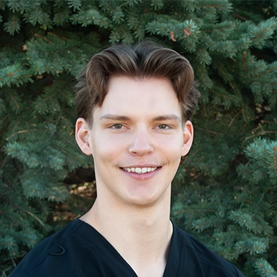 Staff Member At Live Well Chiropractic Conner Smiling In Front Of Fir Tree